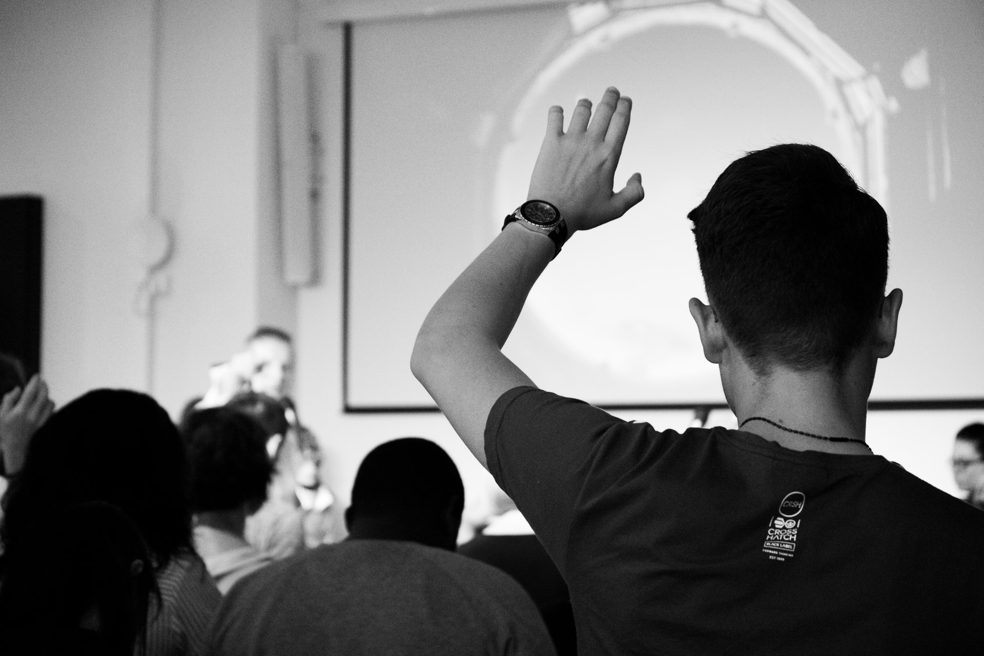Black and white photo set in a classroom. The student in front of you is raising their hand.